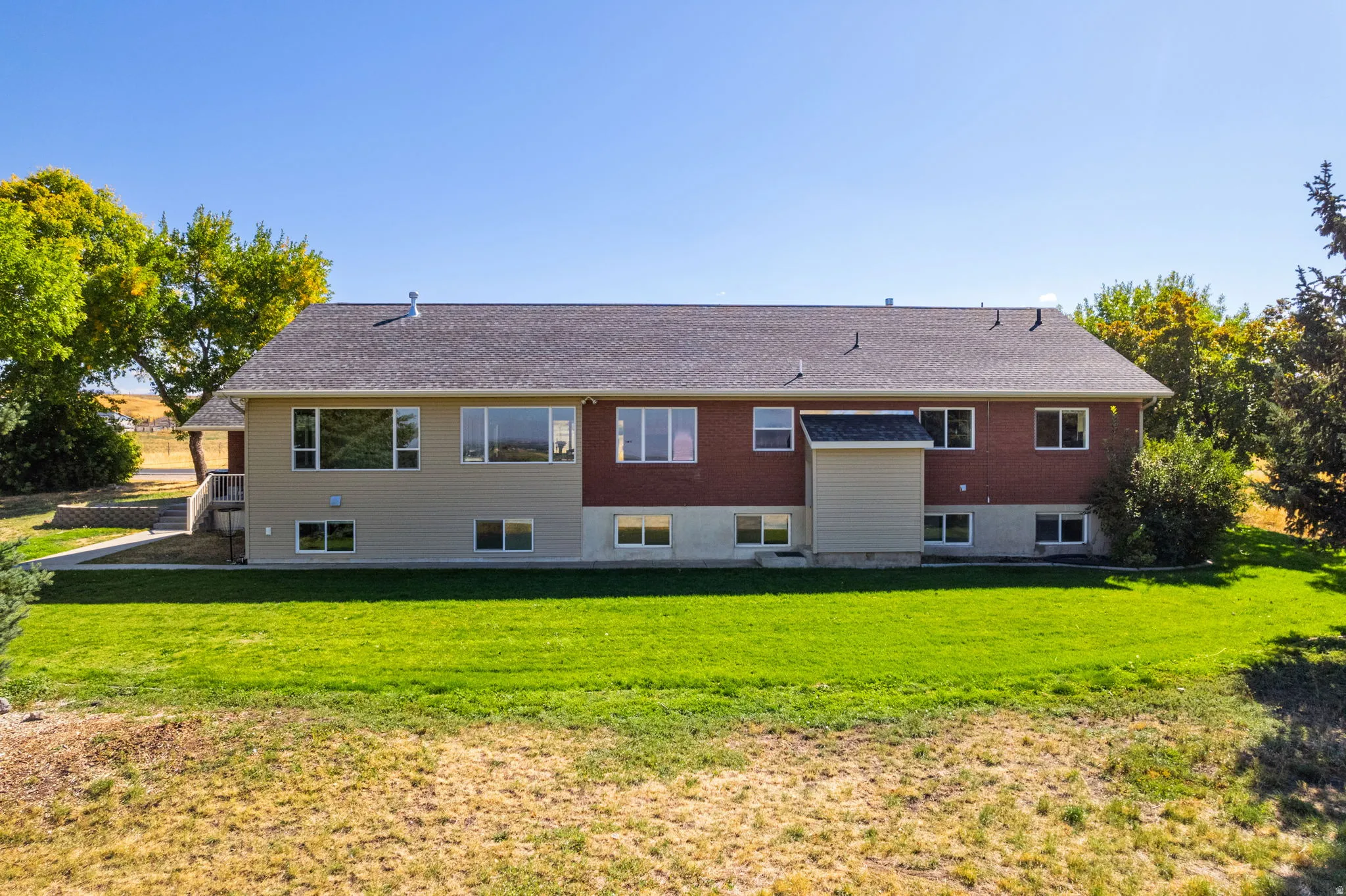 Rear exterior featuring brick and siding finishes, a shingled roof, multiple windows, and a landscaped lawn