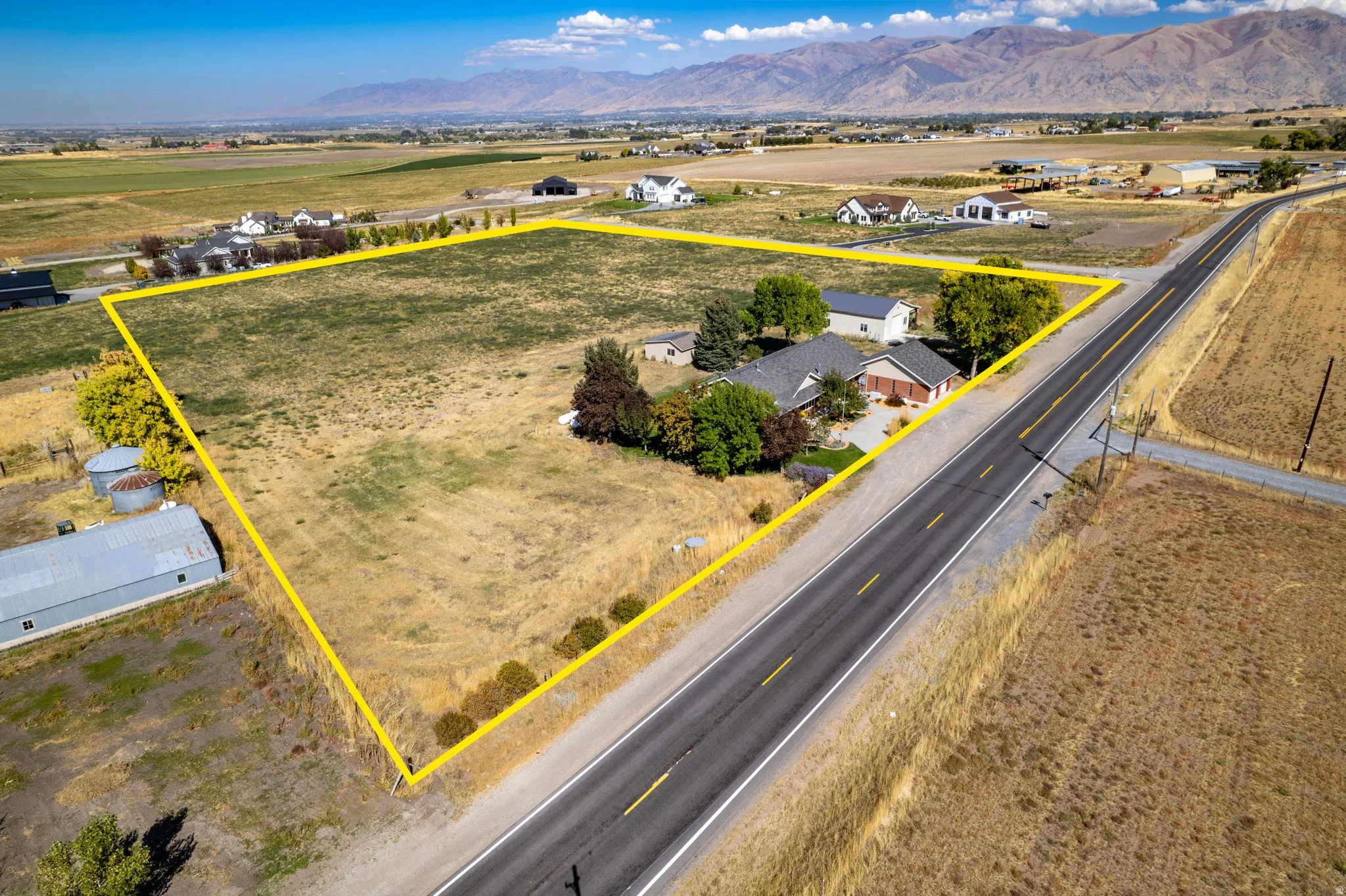 Expansive lot featuring a single-story residence with an attached garage, mature trees, and direct road frontage