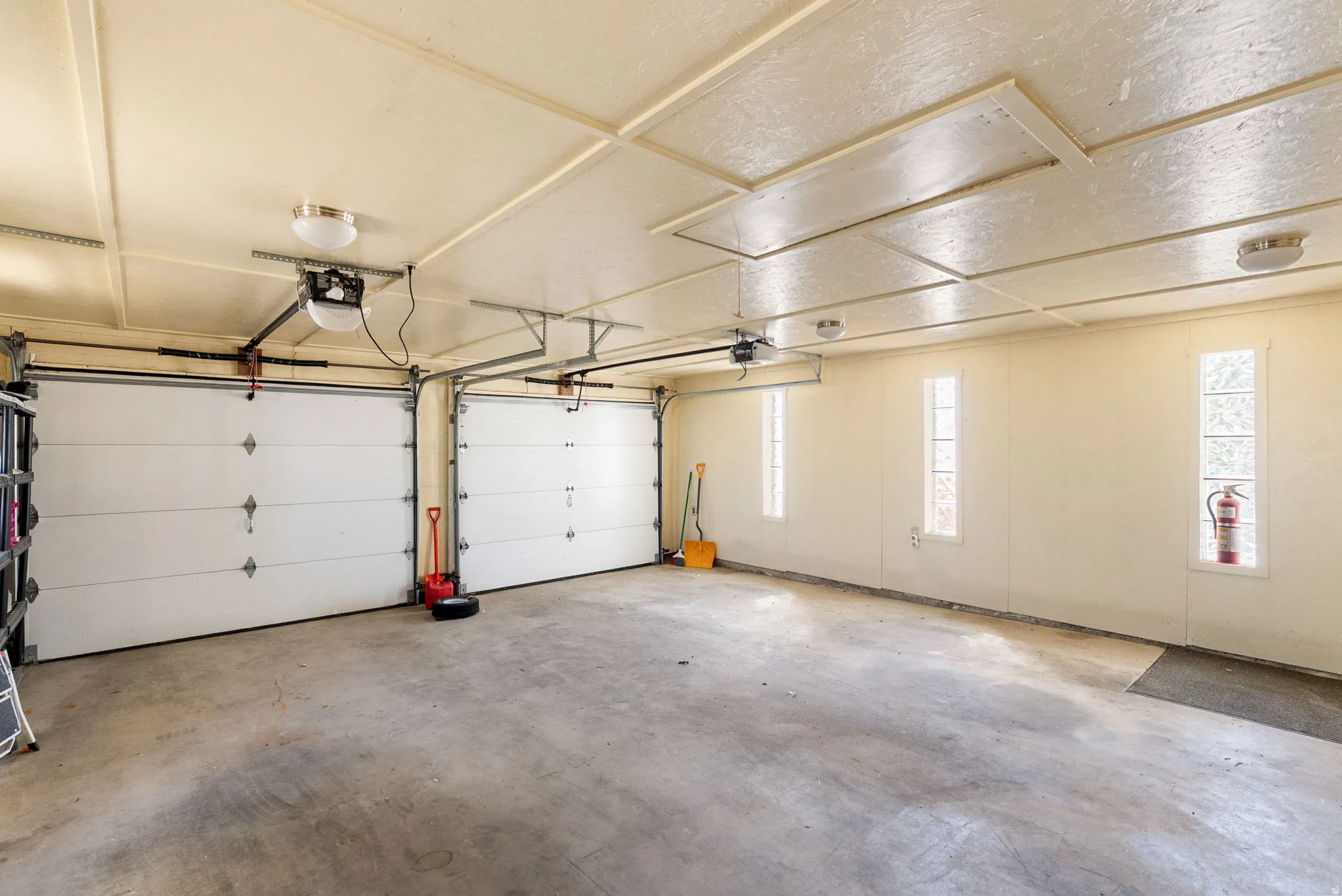 Two automatic garage doors with overhead operating mechanisms, concrete flooring, recessed lighting, and multiple vertical windows
