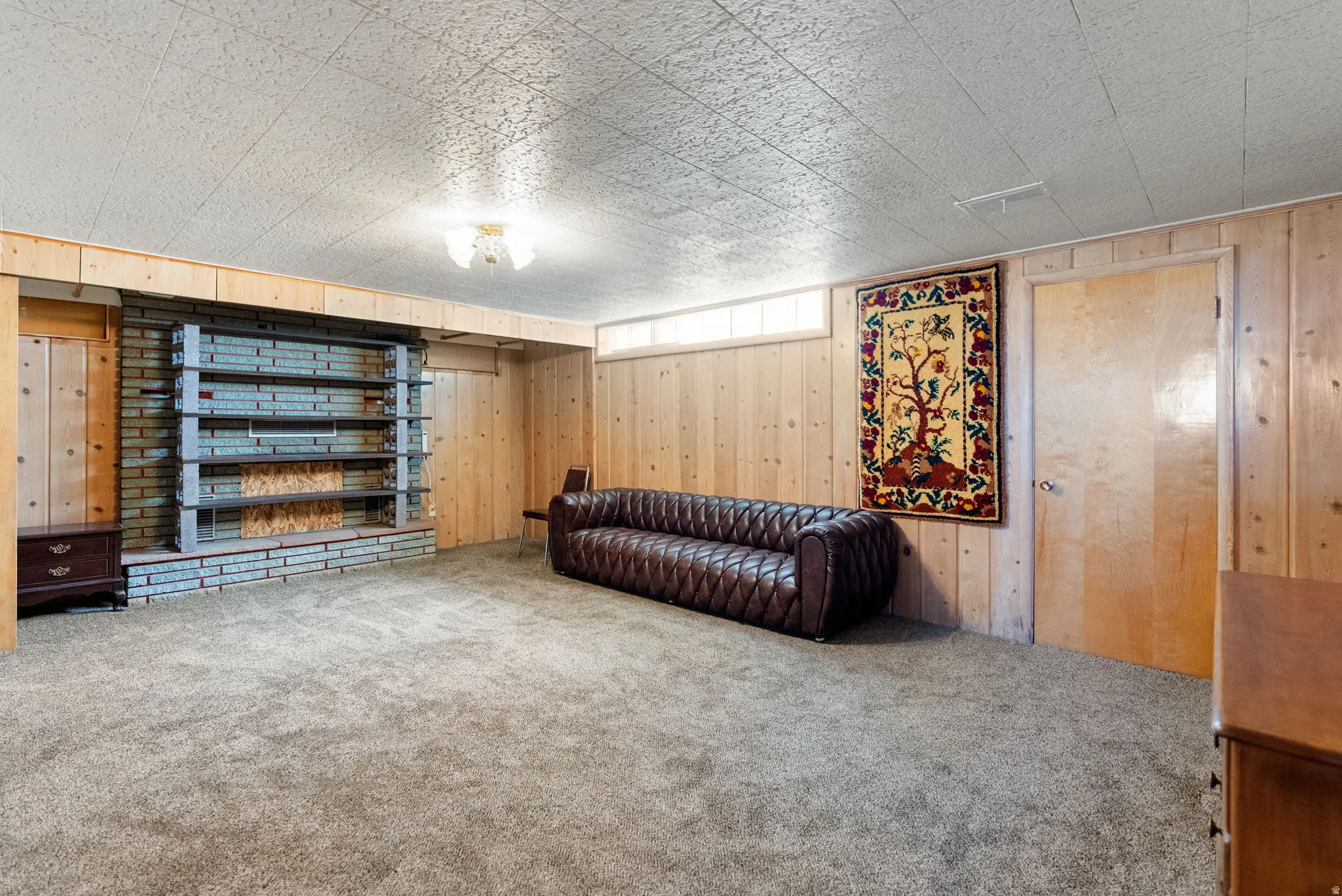 Carpeted room featuring wood paneling, a brick-faced wall with built-in shelving, a wood-finish door, and a textured ceiling