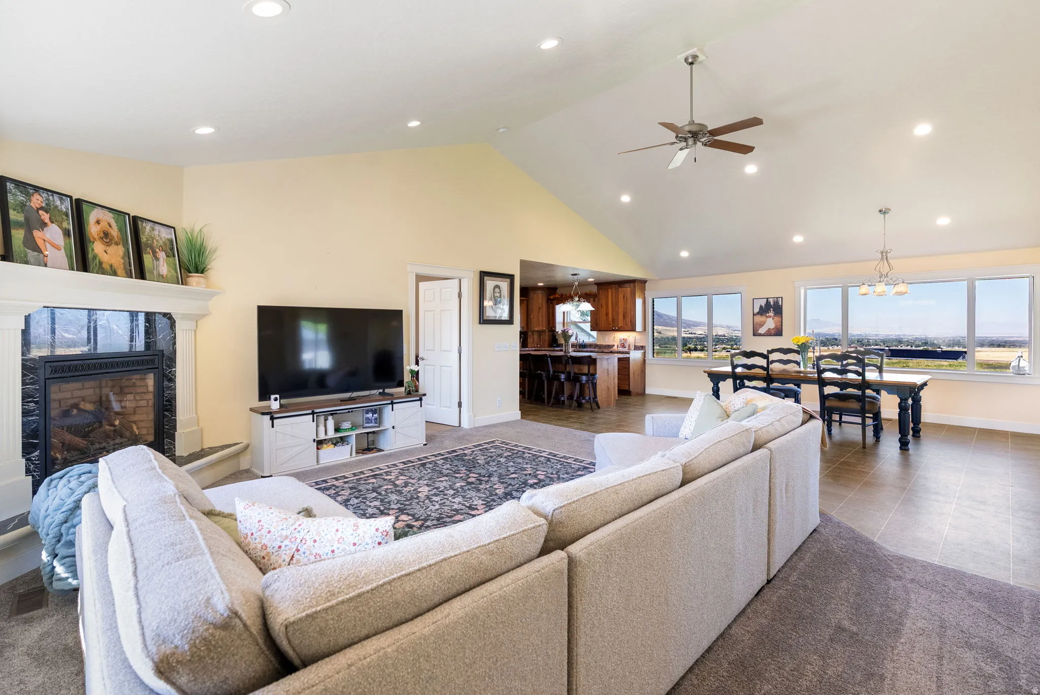 Vaulted ceilings with recessed lighting, fireplace with stone surround, large windows, ceiling fan, and tile flooring