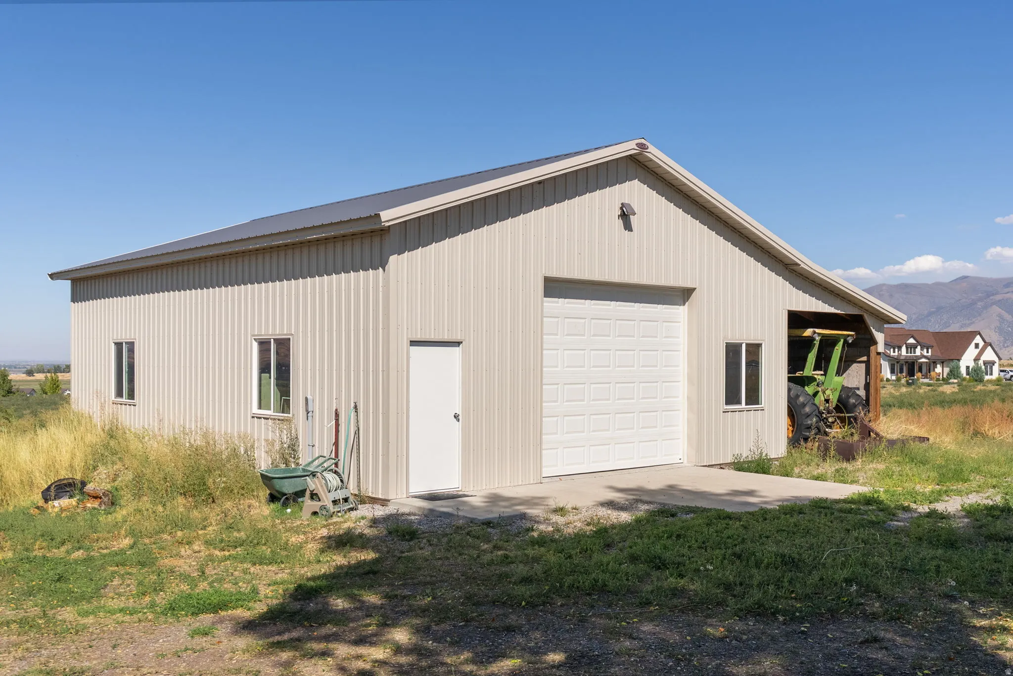 Gable roof structure with metal siding, featuring a paneled garage door, a pedestrian door, and multiple windows