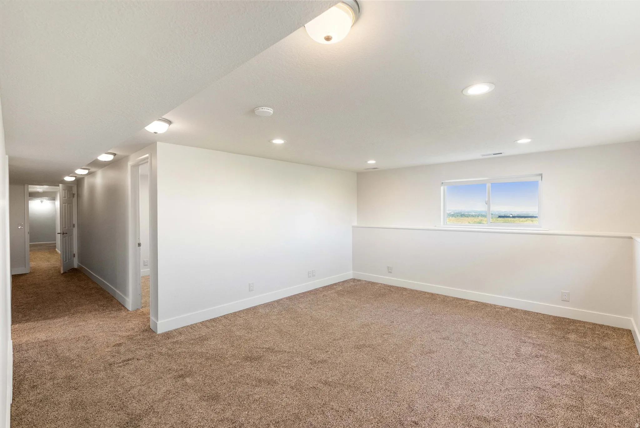 Recessed ceiling lighting, window with exterior scenery, two-tone wall paneling, and neutral-toned carpeting