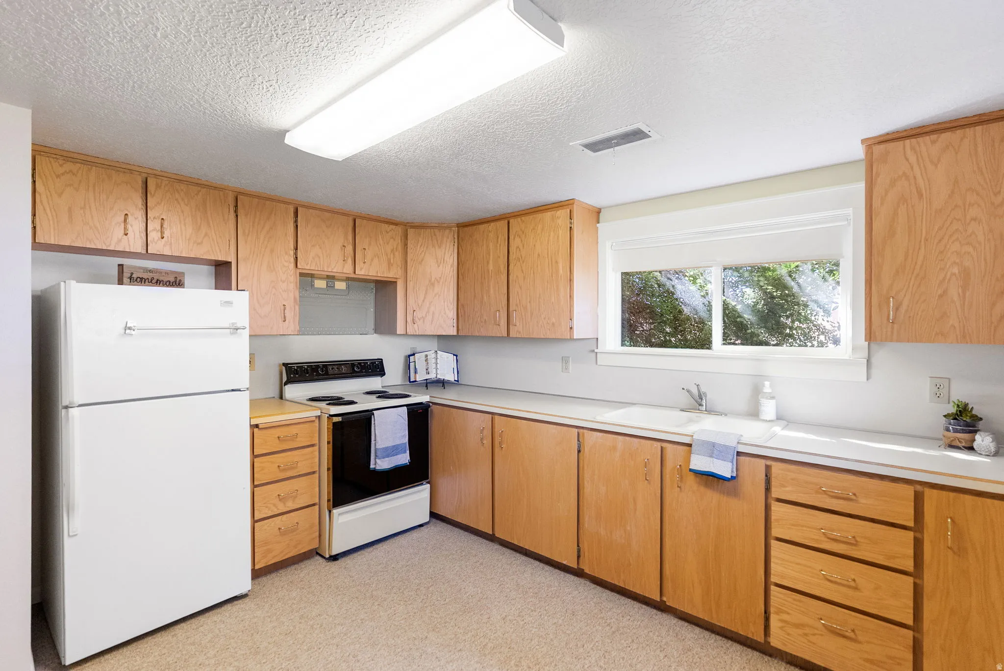 Second kitchen downstairs featuring wood-finish cabinetry, white countertops, a white refrigerator, and a white electric range