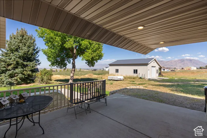 Covered patio with integrated lighting and railing, concrete patio surface, and a detached auxiliary building with a roll-up door