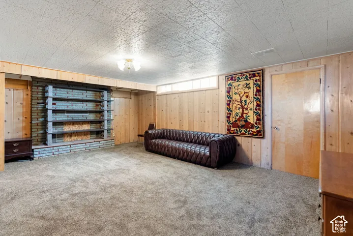 Carpeted room featuring wood paneling, a brick-faced wall with built-in shelving, a wood-finish door, and a textured ceiling