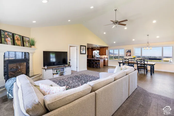 Vaulted ceilings with recessed lighting, fireplace with stone surround, large windows, ceiling fan, and tile flooring