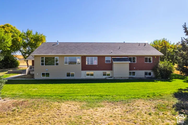 Rear exterior featuring brick and siding finishes, a shingled roof, multiple windows, and a landscaped lawn