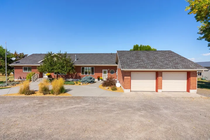 Brick exterior, multi-car attached garage, expansive paved driveway, and mature landscaping