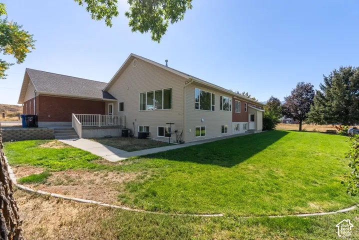 Spacious rear yard with a manicured lawn, an elevated deck with white railing, and a side patio with steps