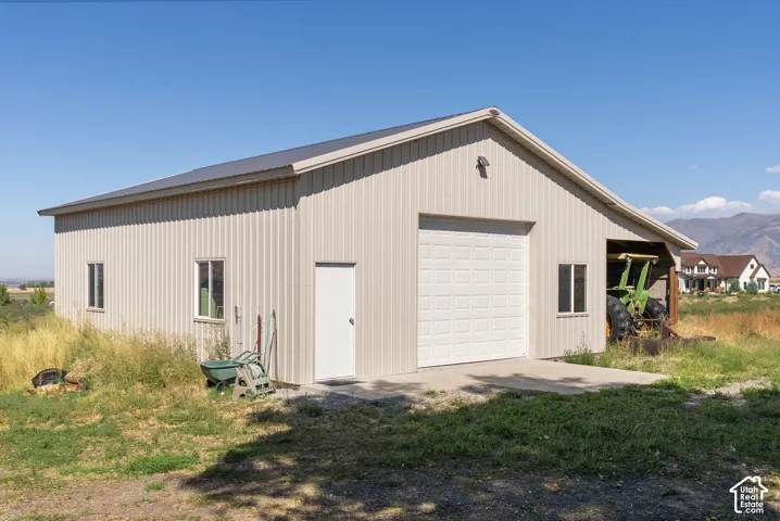 Gable roof structure with metal siding, featuring a paneled garage door, a pedestrian door, and multiple windows