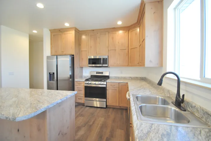 Kitchen featuring wood cabinetry, stainless steel appliances, dual basin sink, and an island with stone countertops