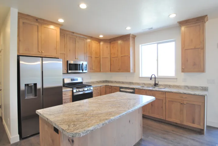 Kitchen featuring wood cabinetry, stainless steel appliances, a center island with a stone countertop, a double basin sink with a gooseneck faucet, and recessed lighting