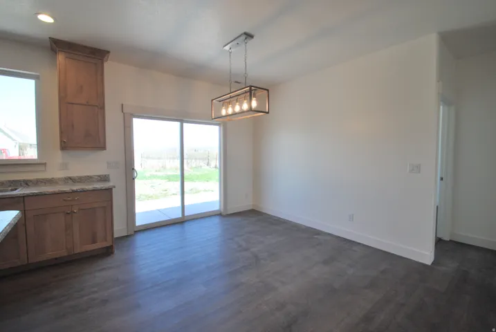 Wood-finish flooring with a modern linear chandelier, wood cabinetry, stone countertops, and a sliding glass door to the exterior