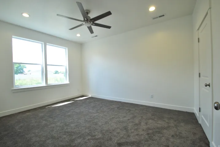 Primary Bedroom with recessed lighting, ceiling fan with brushed nickel finish, two windows, textured carpet, and a paneled door that leads to the walk in closet.