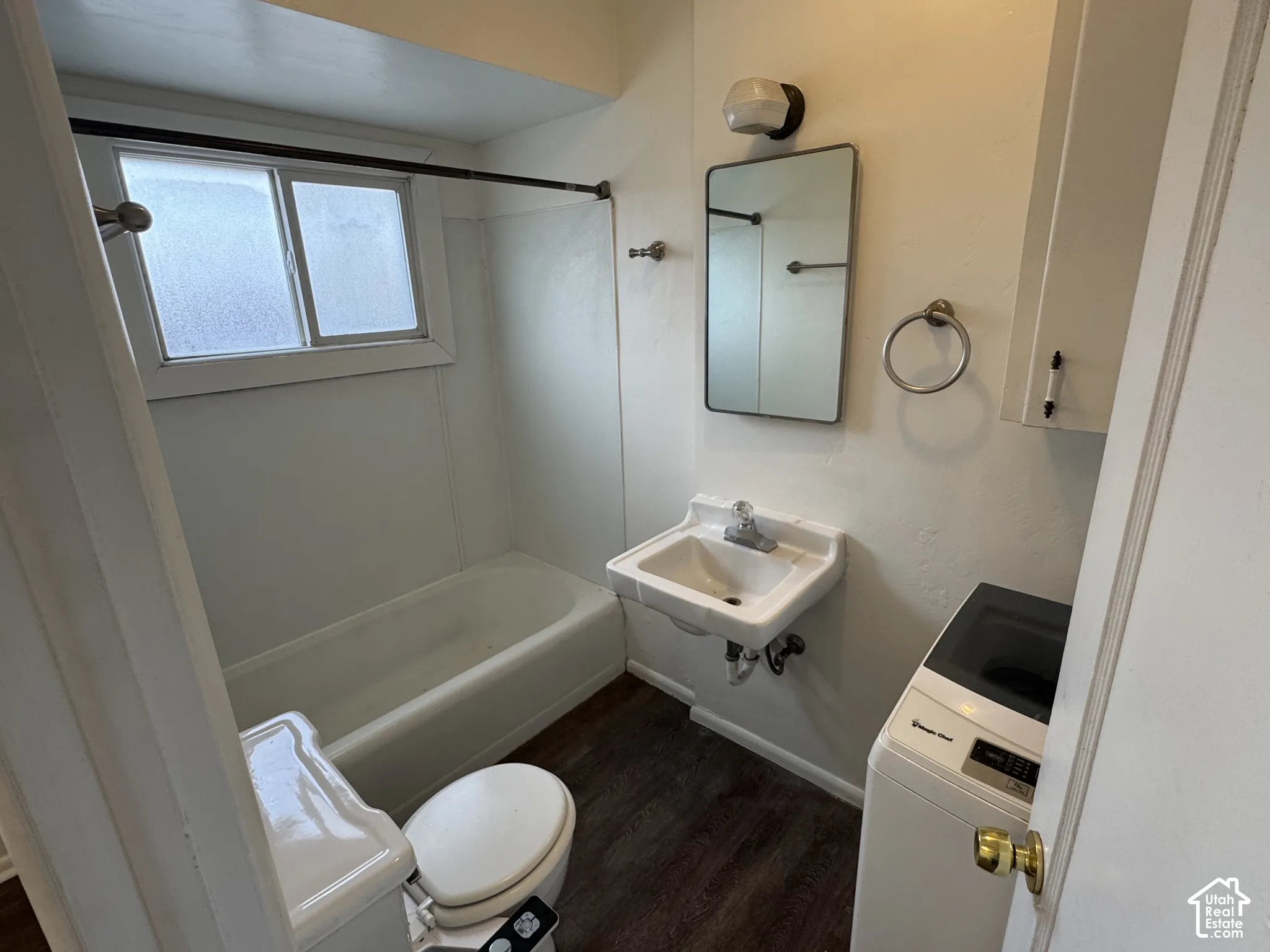 Full bathroom featuring a white tub, wall-mounted sink, built-in wall cabinet, and wood-finish flooring