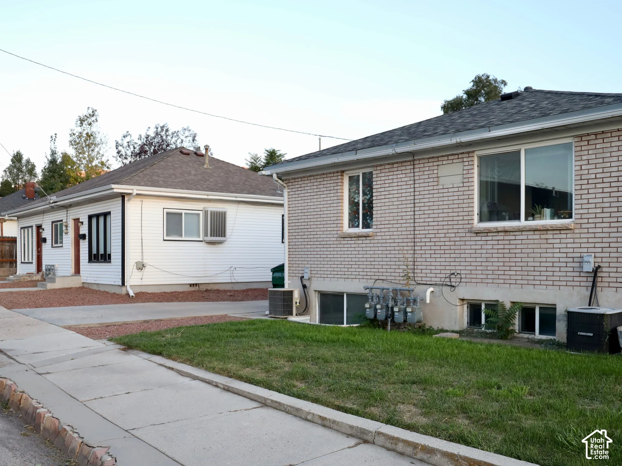 Two residential structures, one with light-colored brick siding and another with white horizontal siding and dark-trimmed windows