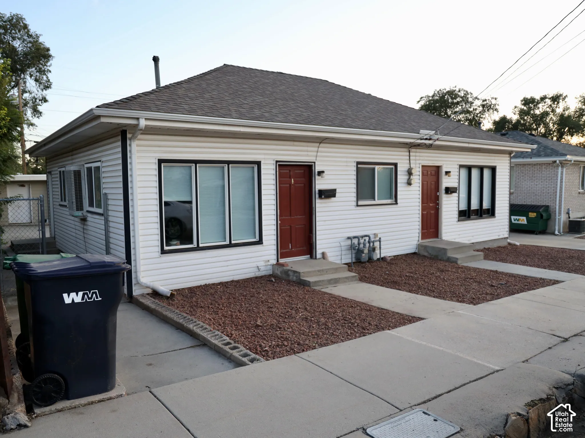 Duplex property featuring white siding, a dark shingle roof, two distinct entry doors, and individual concrete walkways