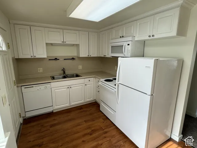 Kitchen featuring white cabinetry, light-toned countertops, a double basin sink, wood-finish flooring, and white appliances