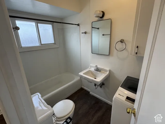 Full bathroom featuring a white tub, wall-mounted sink, built-in wall cabinet, and wood-finish flooring