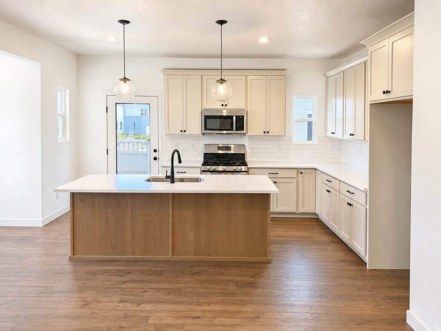 Wood-finish flooring, central island with an integrated sink, cream-colored cabinetry, stainless steel appliances, and subway tile backsplash