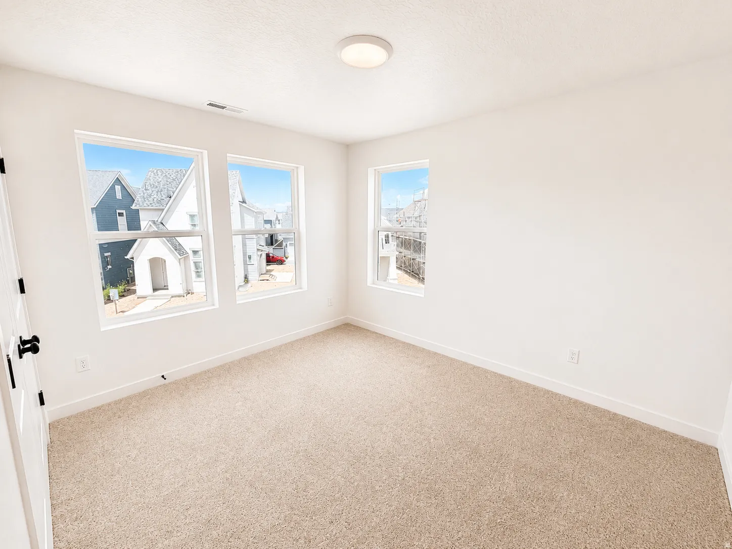 Neutral tone carpeting, three windows with white frames, white interior walls, white ceiling, and a flush-mount ceiling light fixture