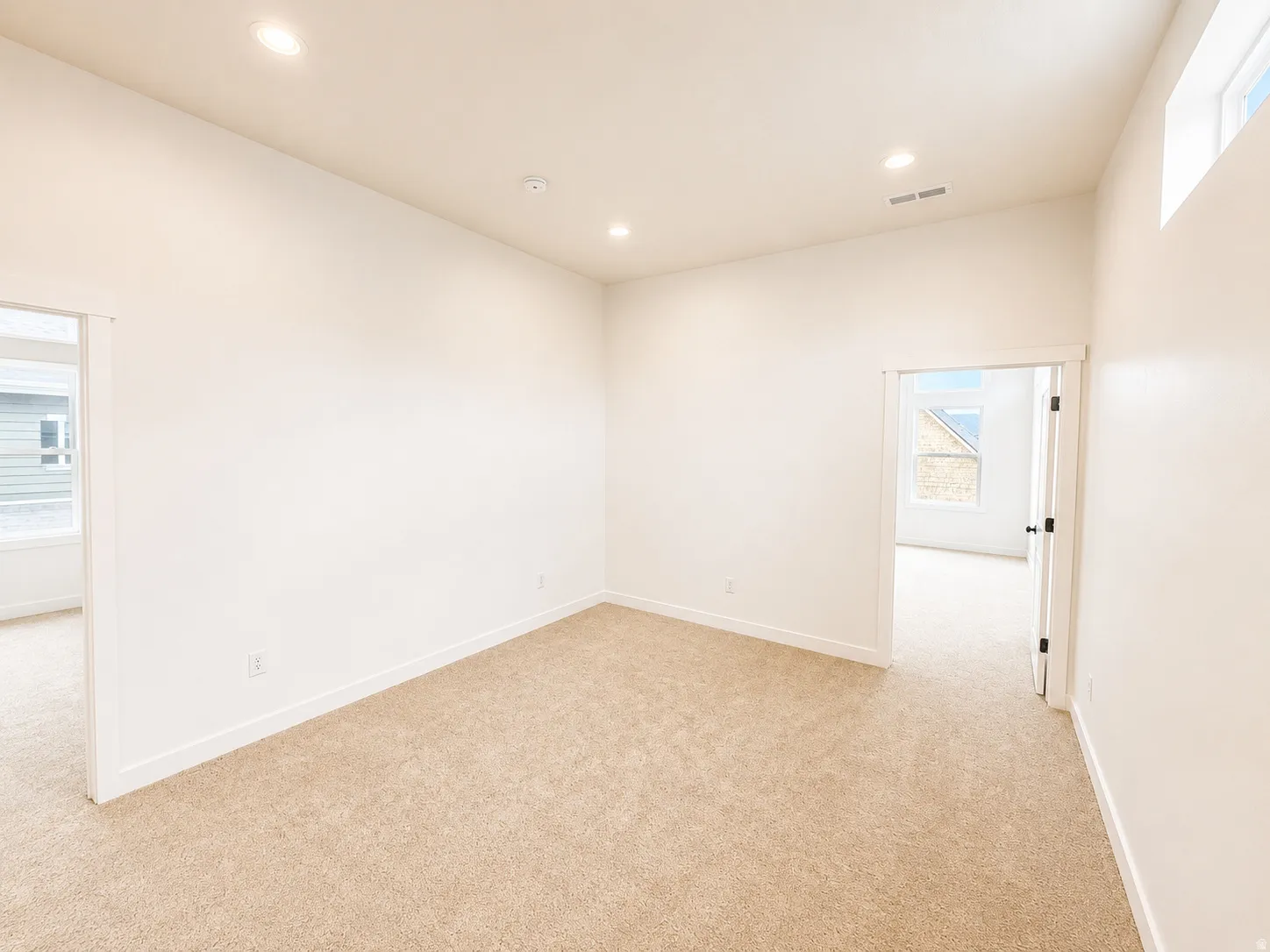 Neutral-toned carpeting, recessed ceiling lighting, high ceilings, and a high window