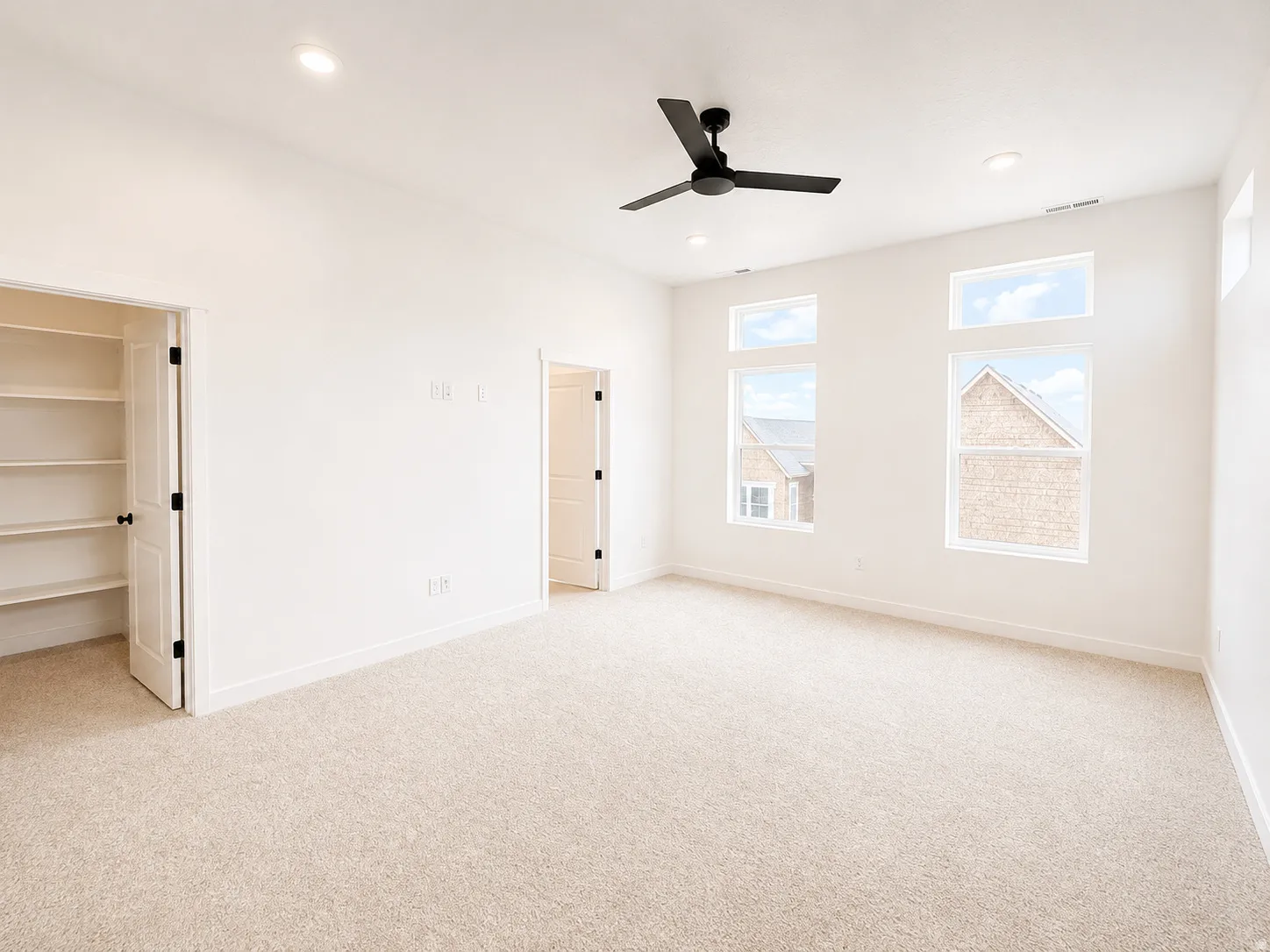 Spacious room with light-toned carpeting, ample natural light from multiple windows, recessed lighting, and a ceiling fan