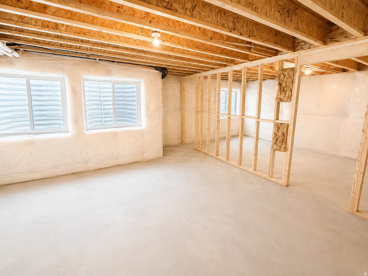 Unfinished basement with exposed wood framing, concrete flooring, and two window wells