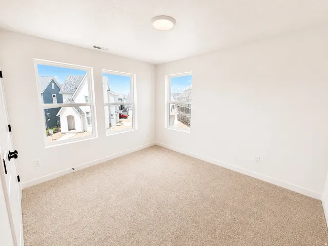 Neutral tone carpeting, three windows with white frames, white interior walls, white ceiling, and a flush-mount ceiling light fixture
