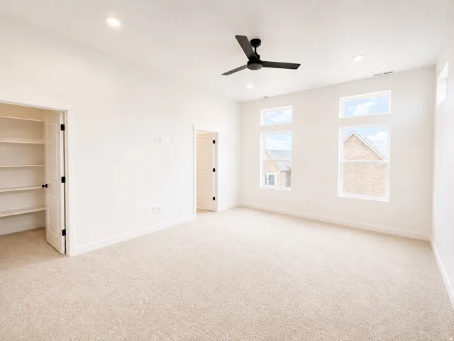 Spacious room with light-toned carpeting, ample natural light from multiple windows, recessed lighting, and a ceiling fan