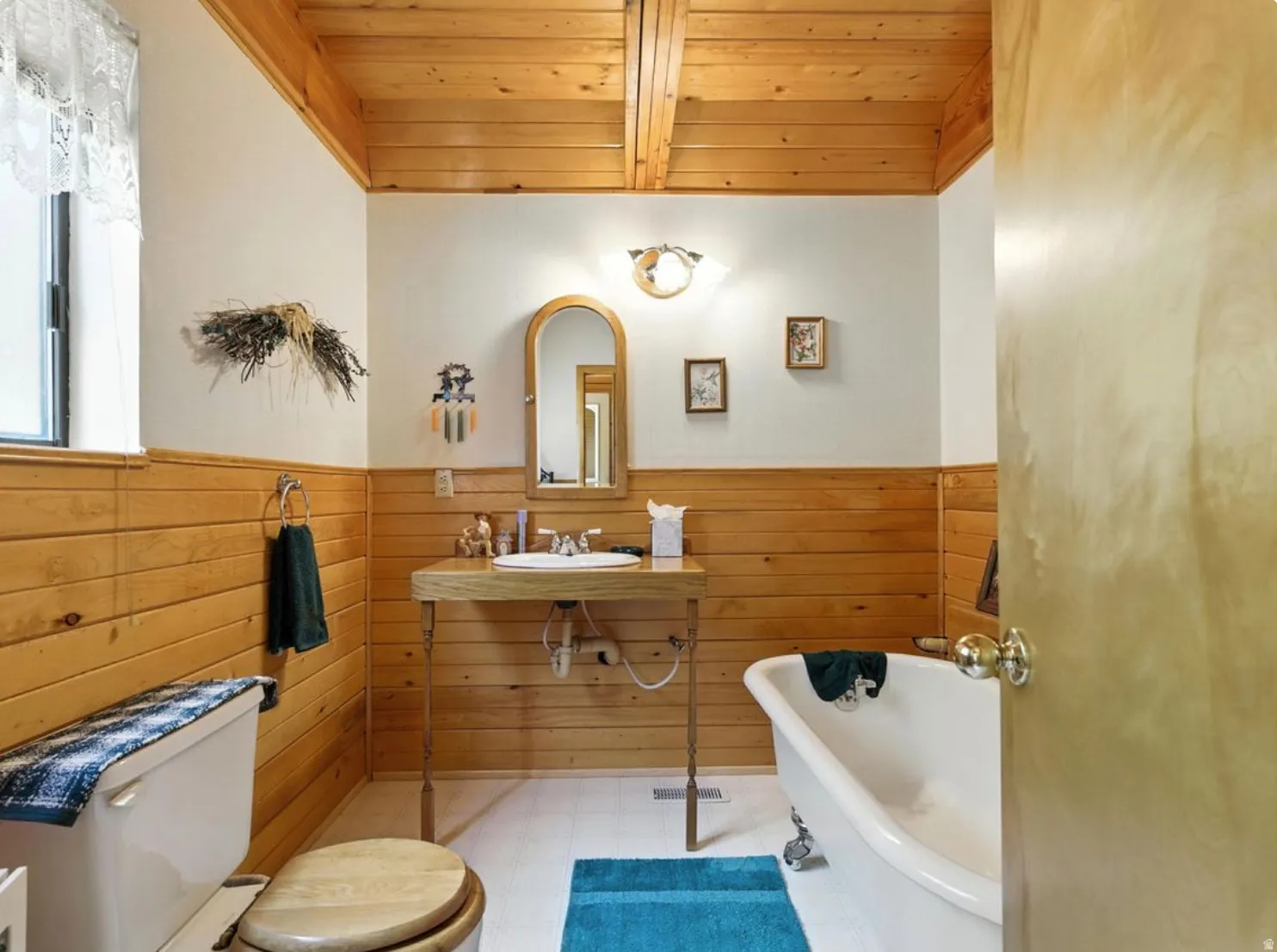 Wood-paneled walls and ceiling beams, freestanding vanity with integrated sink, and a clawfoot tub