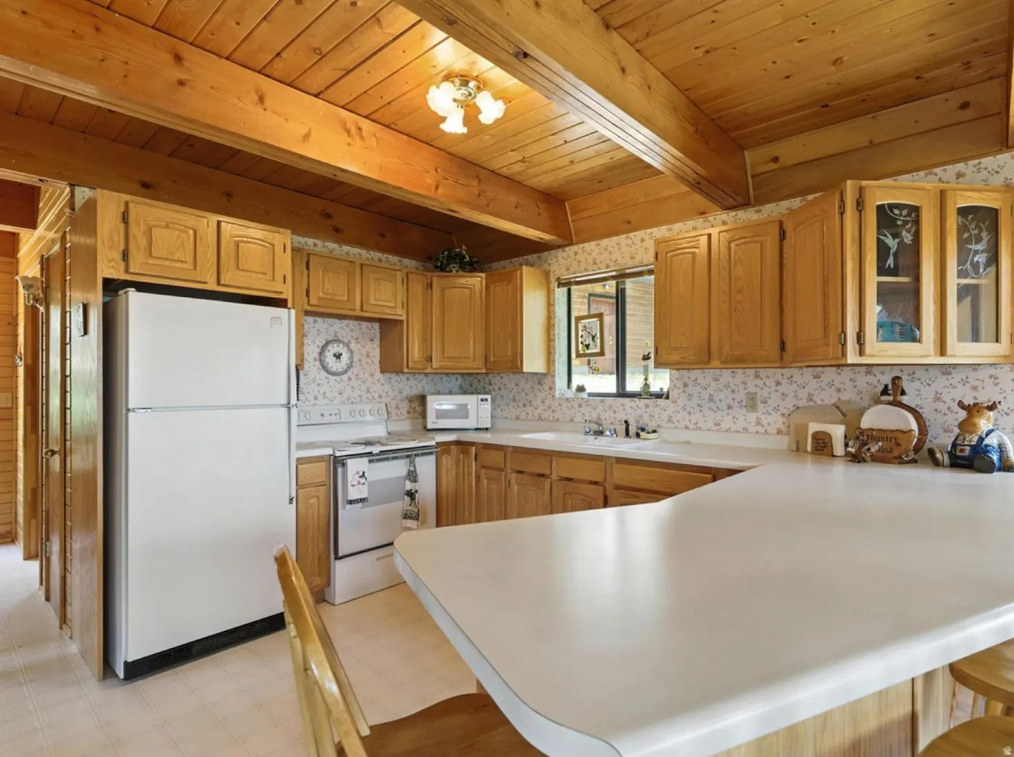 Wood-panel vaulted ceiling with exposed beams, wood-finish cabinetry, white countertops, built-in sink, and white appliances
