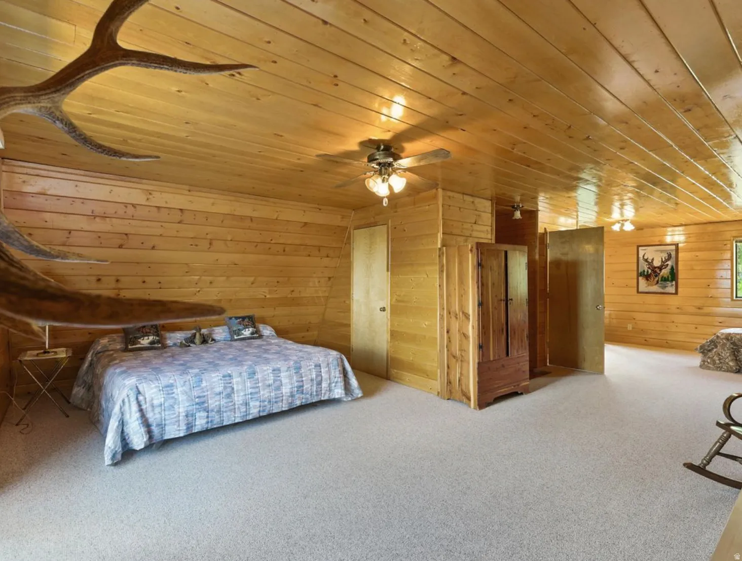 Wood-paneled walls and ceiling, ceiling fans, built-in wooden cabinetry, and neutral carpeting