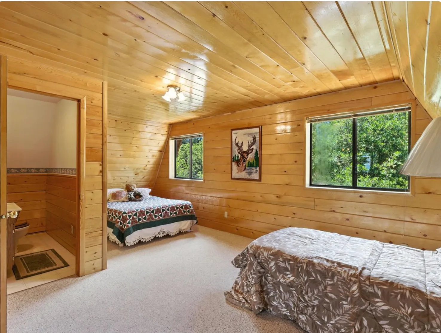 Sloping wood-paneled ceiling with recessed lighting, wood-paneled walls, two distinct window openings, and light-colored carpeting