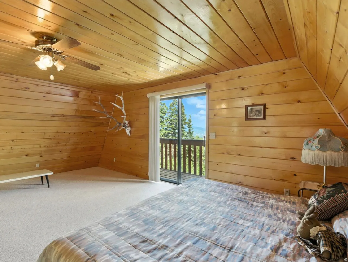 Vaulted wood-paneled ceiling, wood-paneled walls, carpeted flooring, and a sliding glass door to a private balcony