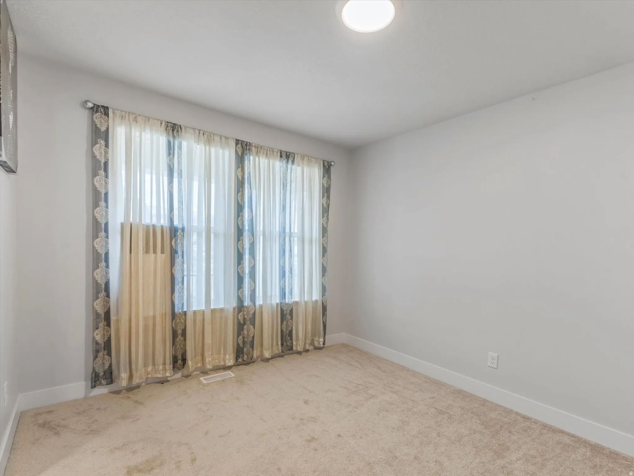 Recessed window with sheer and patterned drapes, flush-mount ceiling light, and light-toned carpet flooring