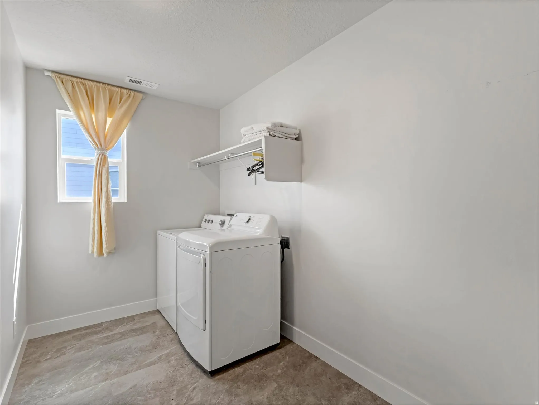 Dedicated laundry area featuring a window, overhead shelving, and durable flooring