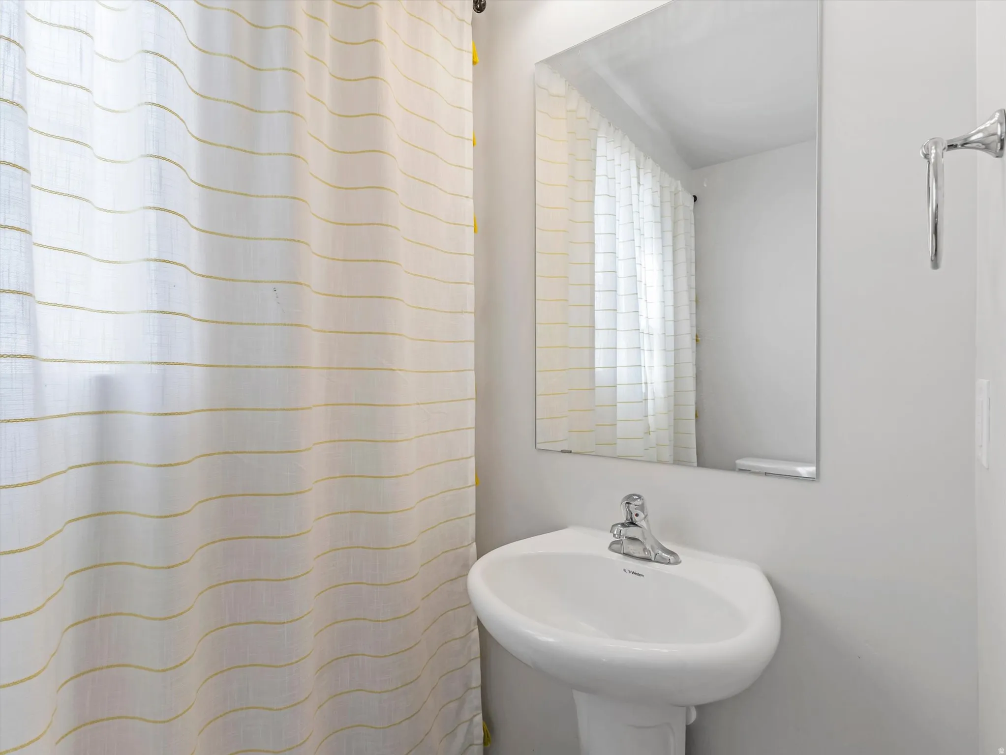Pedestal sink with chrome faucet, wall-mounted mirror, and chrome towel bar