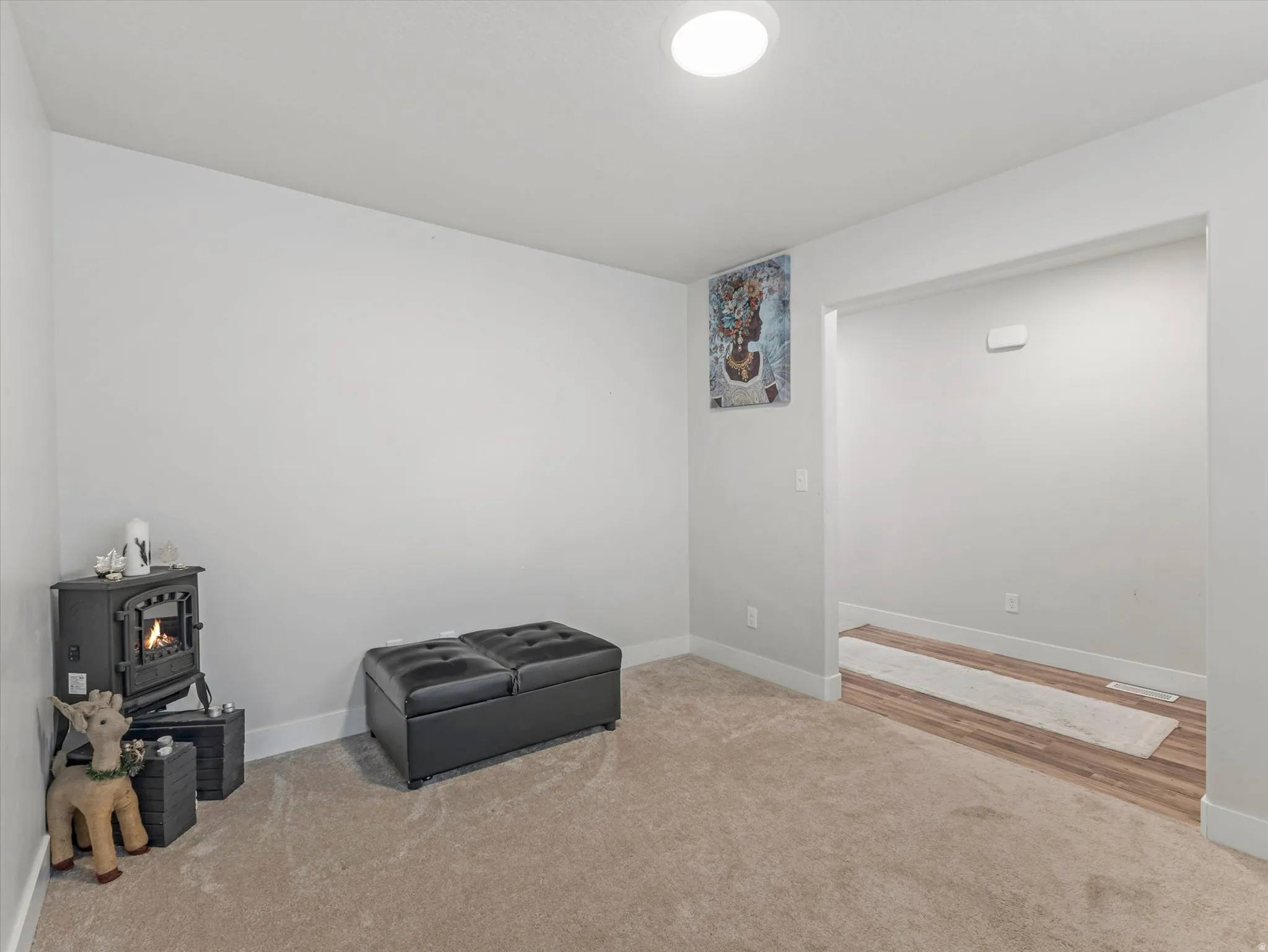 Carpeted room with a built-in ceiling light, a corner fireplace unit, and an entryway to a space with wood-finish flooring