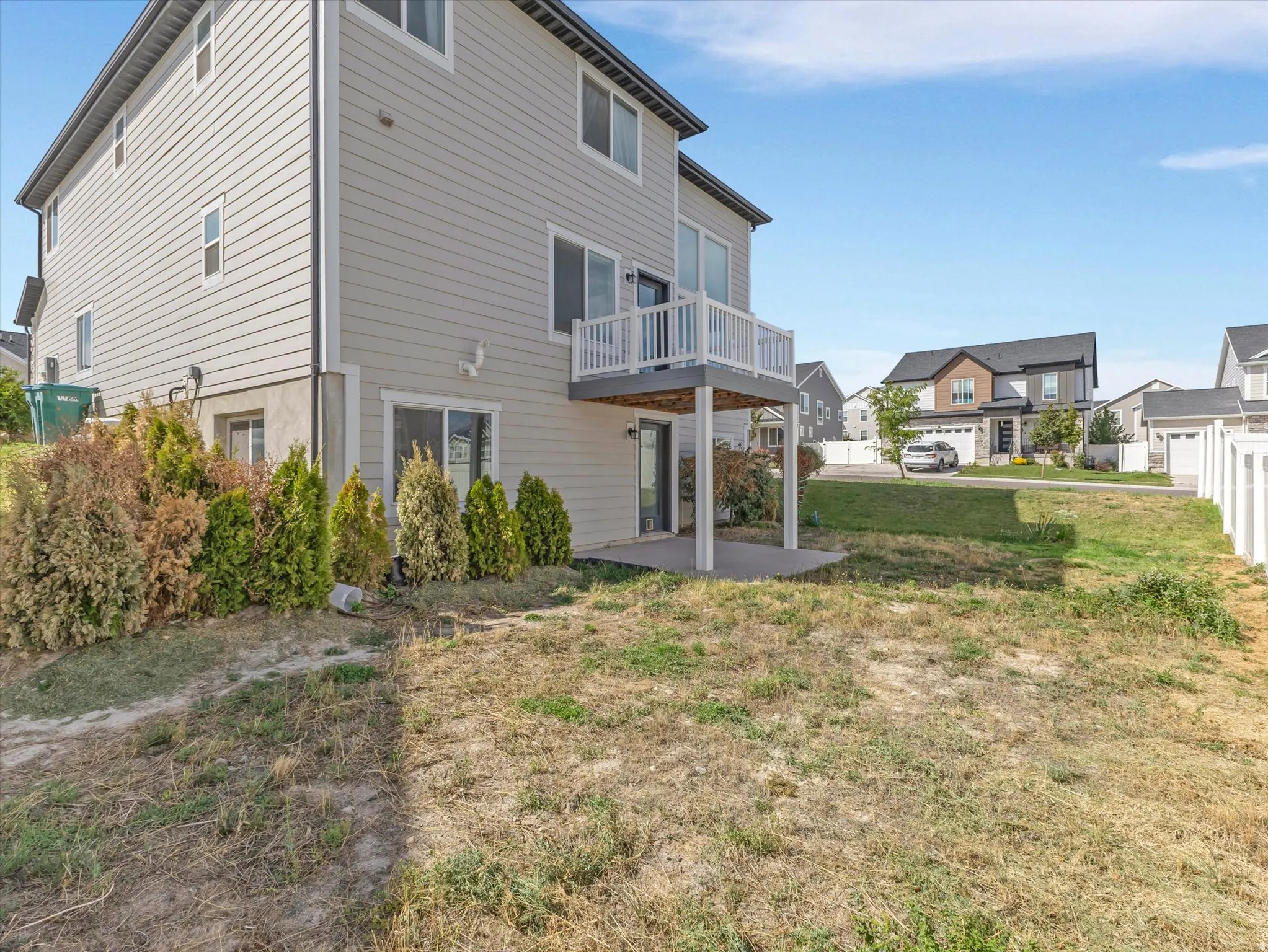 Two-story exterior with light-toned siding, a second-story deck with white railing, and a ground-level concrete patio