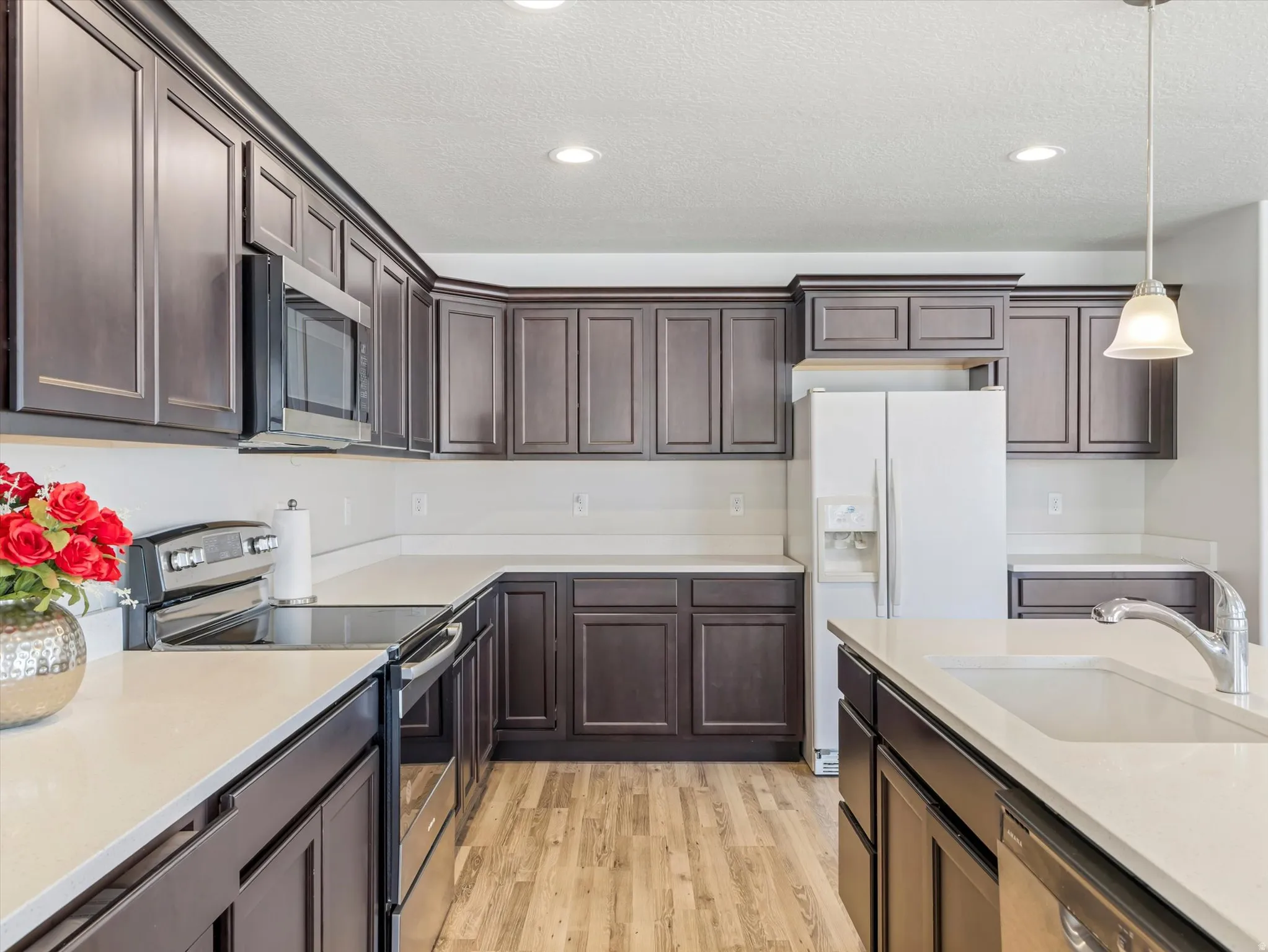 Kitchen featuring dark wood cabinetry, light countertops, wood-finish flooring, stainless steel appliances, and an island with an integrated sink