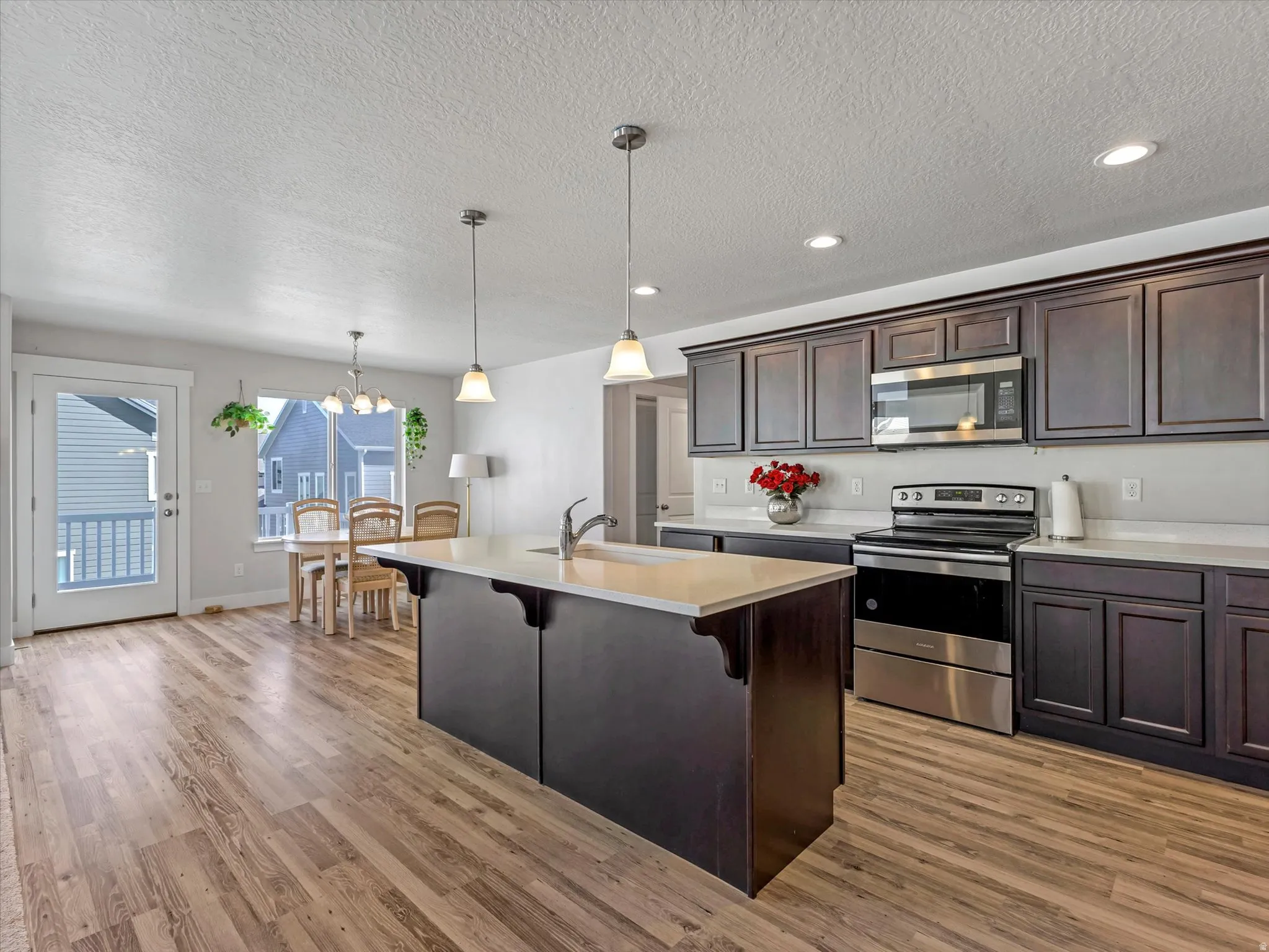 Kitchen featuring dark wood-finish cabinetry, stainless steel appliances, a center island with a sink, and pendant lighting
