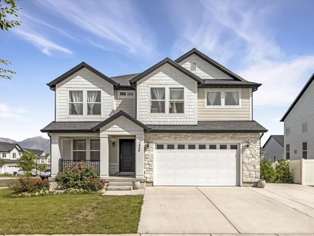 Traditional-style exterior with stone and shingle accents, a covered front porch, an attached two-car garage, and a concrete driveway