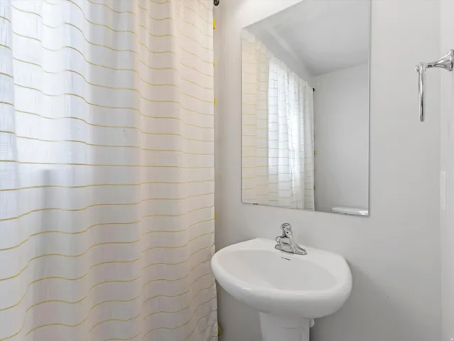 Pedestal sink with chrome faucet, wall-mounted mirror, and chrome towel bar