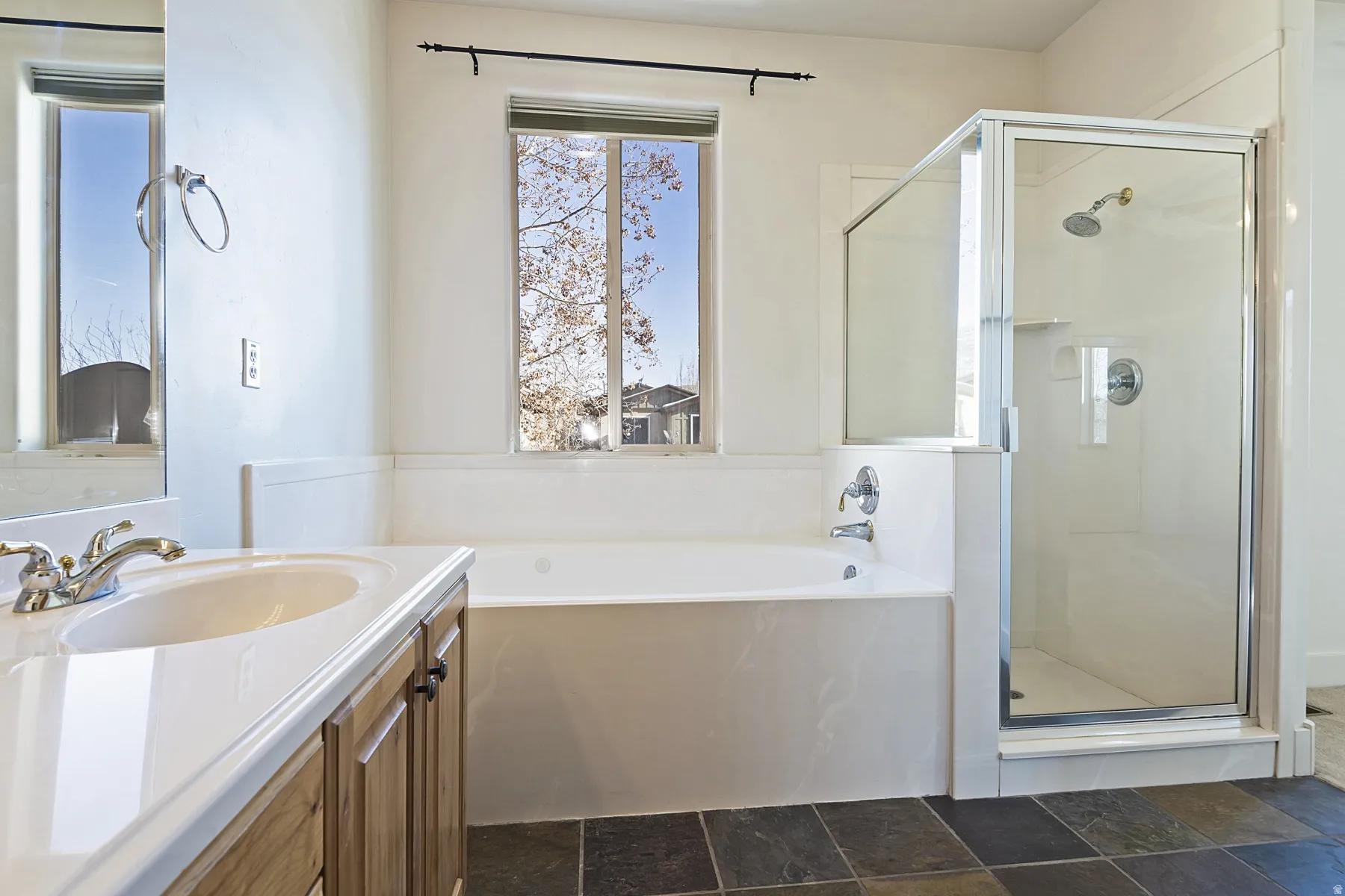 White vanity with integrated sink, chrome fixtures, built-in bathtub, glass-enclosed shower, and dark stone-finish tile flooring