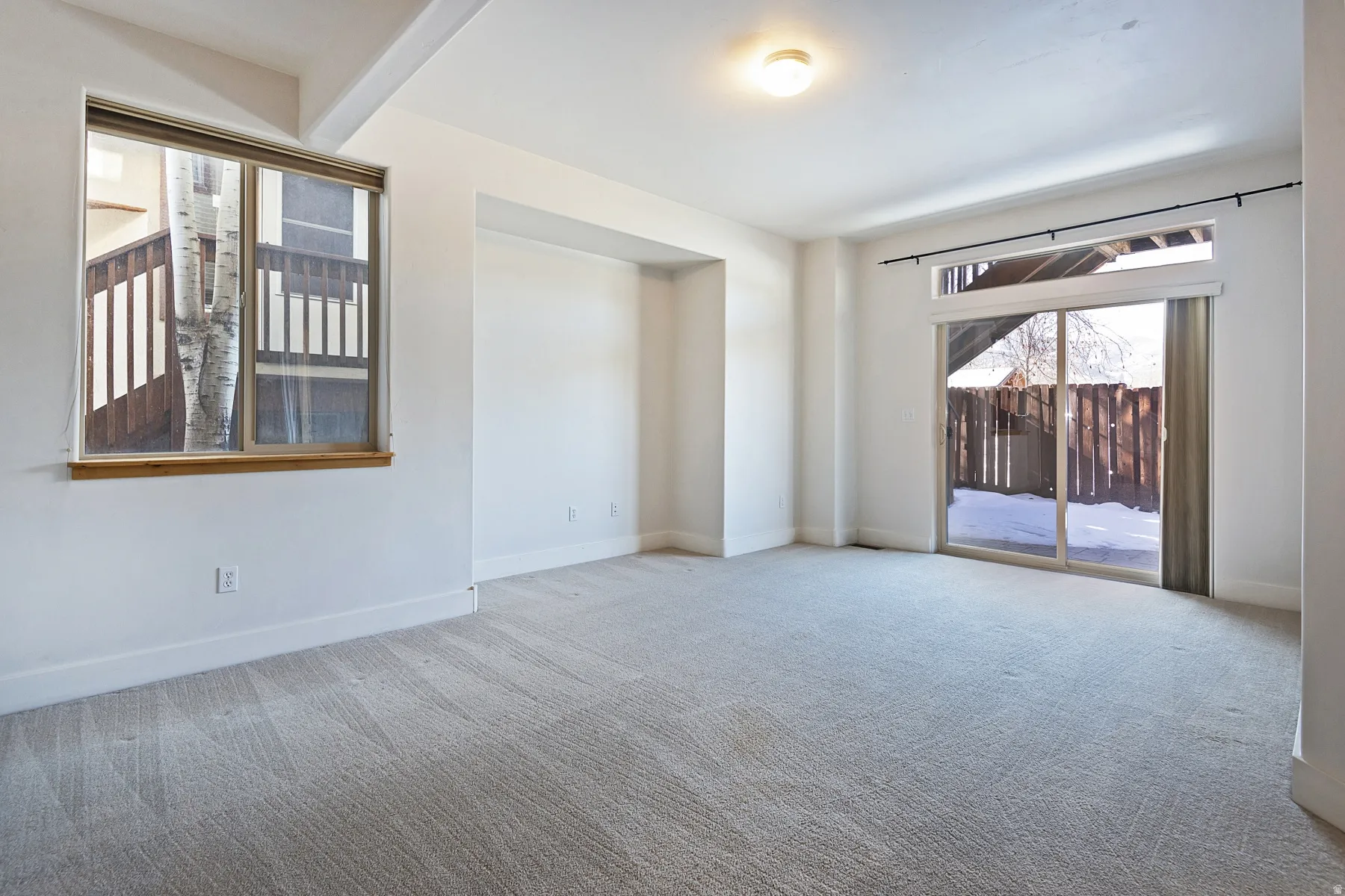Expansive room featuring light gray carpeting, a large sliding glass door, and a prominent window with a wood sill