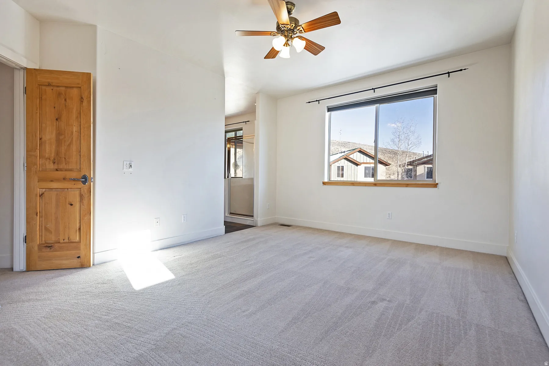 Neutral-toned carpeting, natural wood-finish door, and a ceiling fan with light fixture