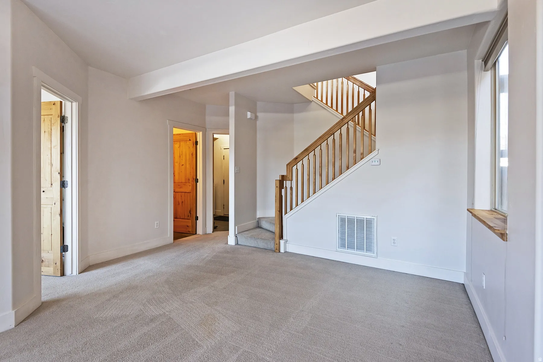 Carpeted flooring, white painted walls, wood staircase, wood doors, and a window with a wood sill