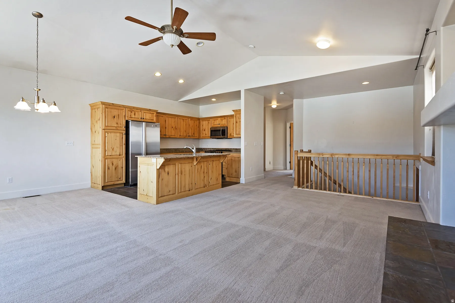 Vaulted ceilings with recessed lighting, wood-finish cabinetry, stainless steel appliances, kitchen island with breakfast bar, and wood banister
